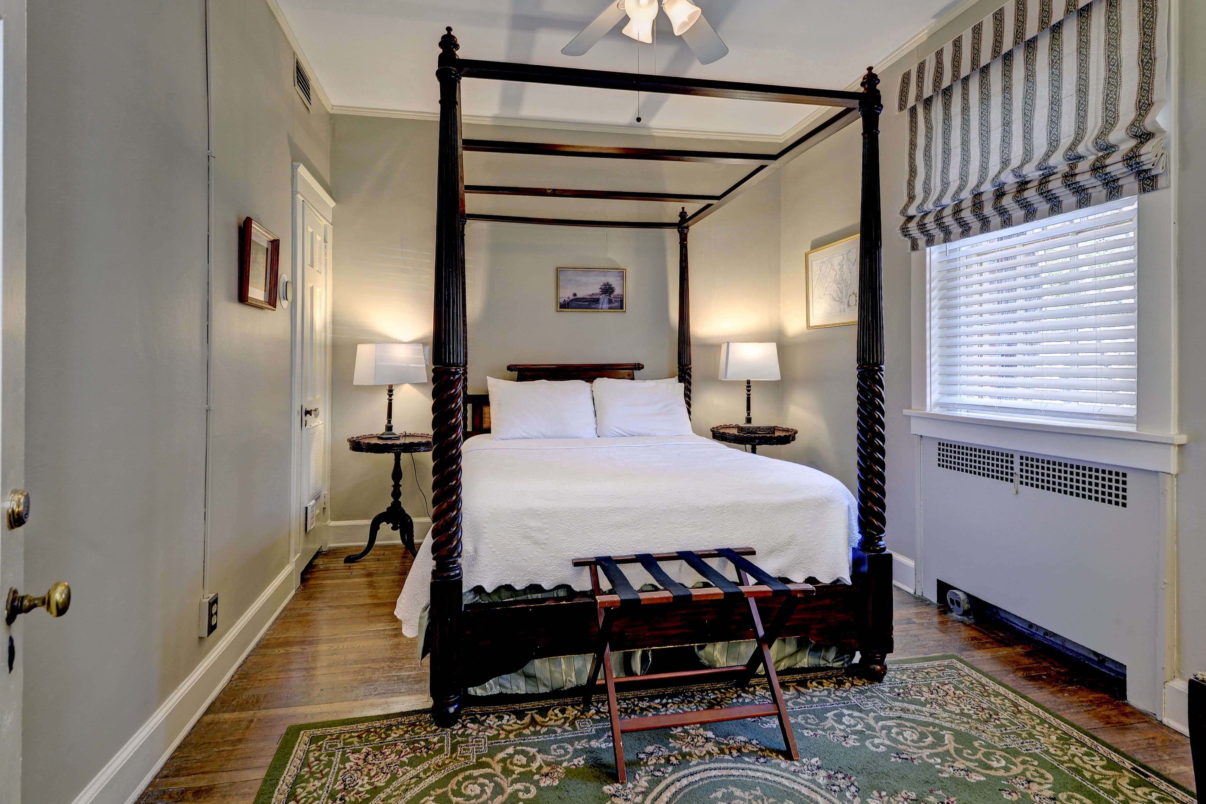 Bedroom in tranquil shades of blue, cream, and white with four-poster bed, cozy armchair, and ceiling fan