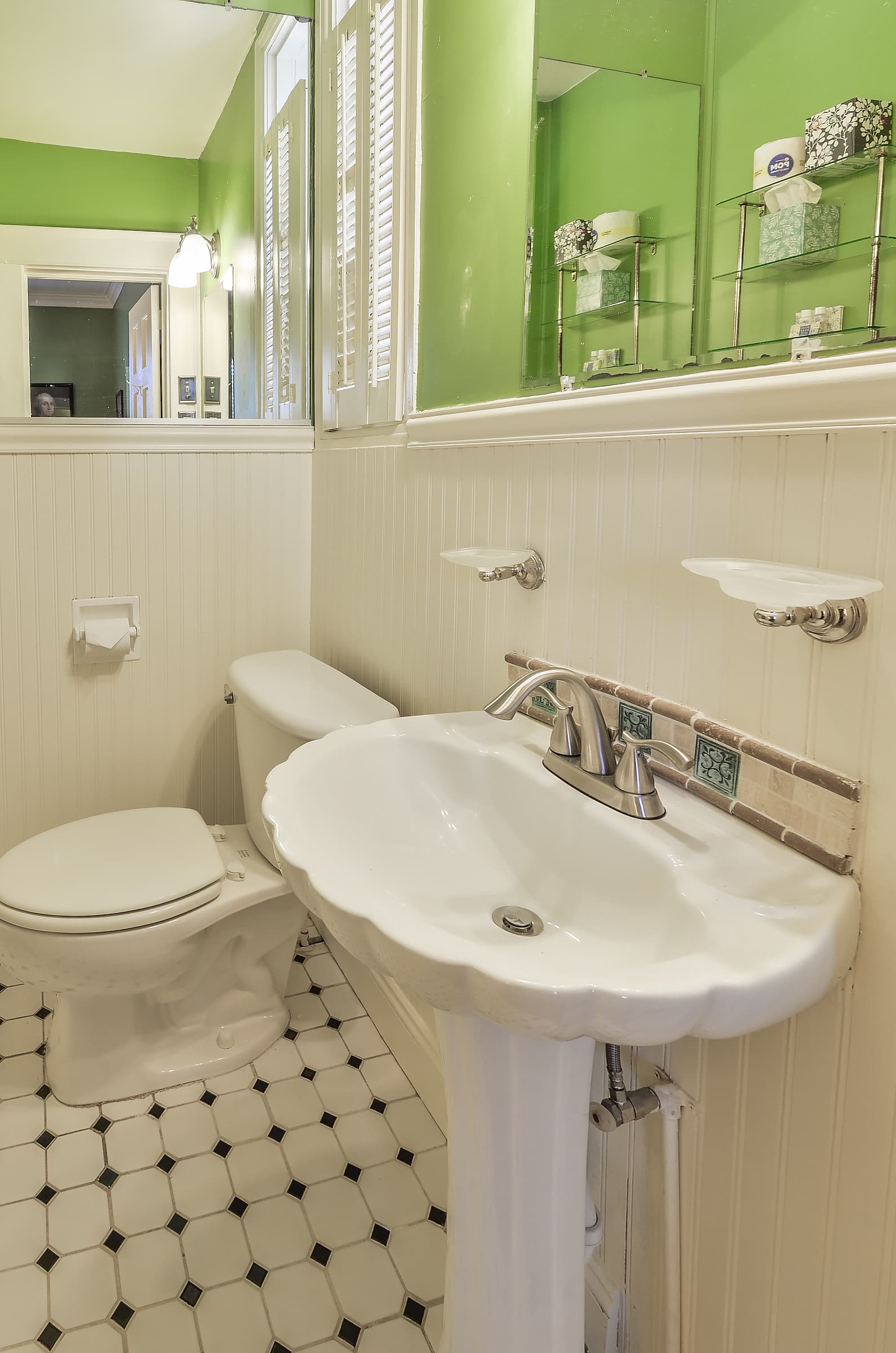 Bathroom with small black and white tile pattern, pedestal sink with decorative scalloped edge, white wainscoting and green walls