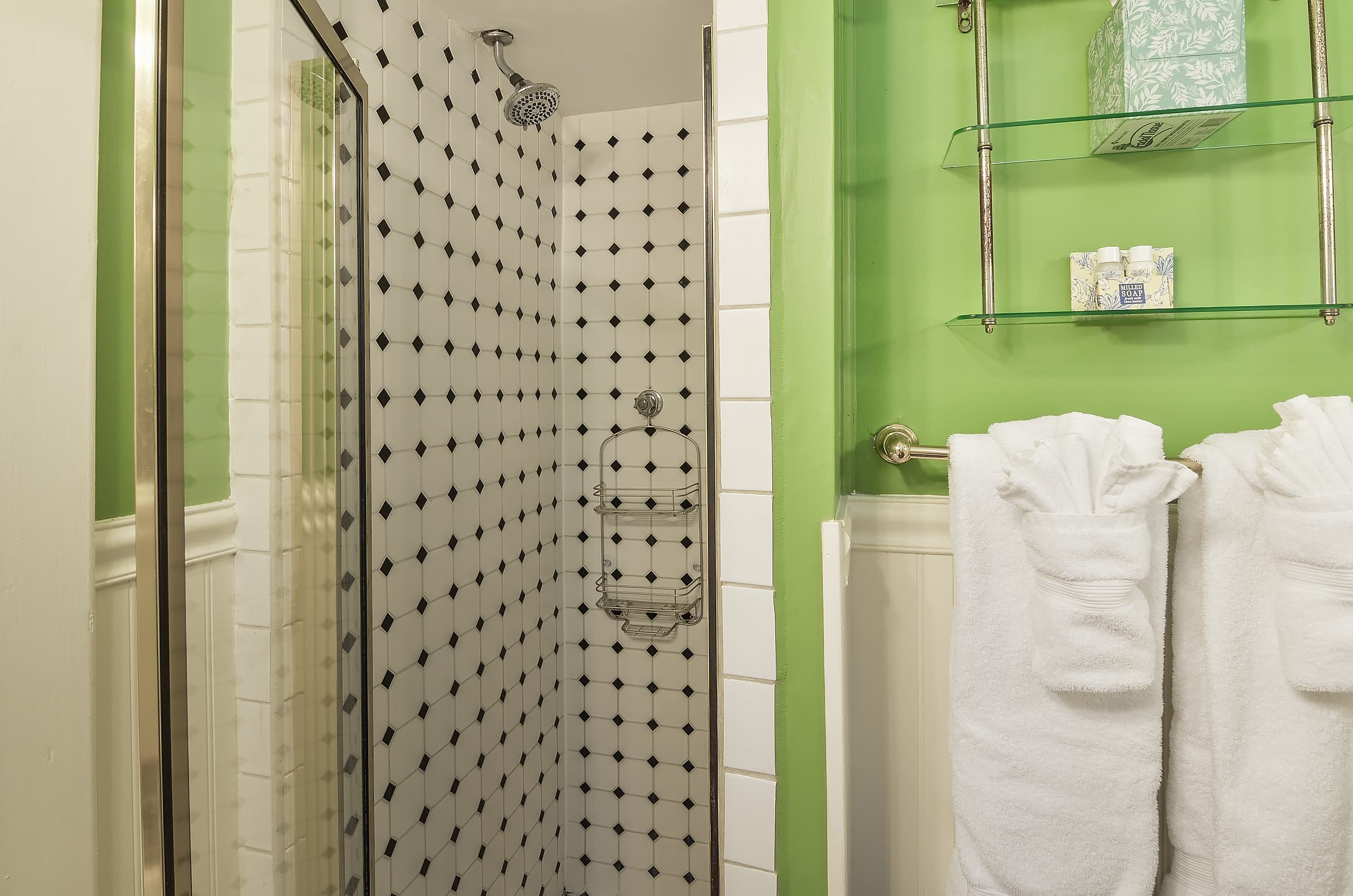 Bathroom with green walls, towels on rack, and a black and white tiled walk in shower