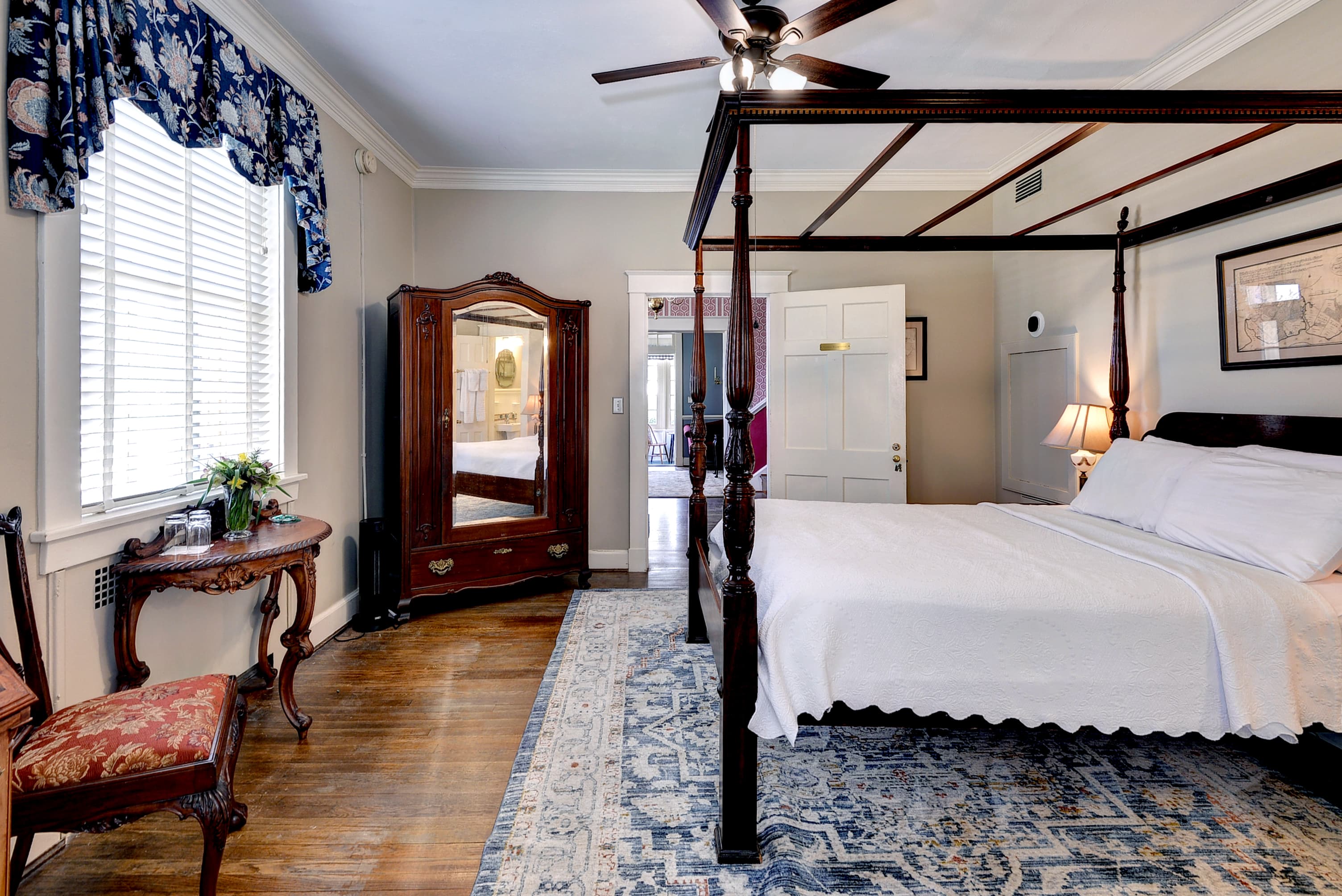 Bedroom with carved mahogany four-poster bed with nightstands and lamps, ornate oriental rug, antique armoire with full length mirror, and green painted walls
