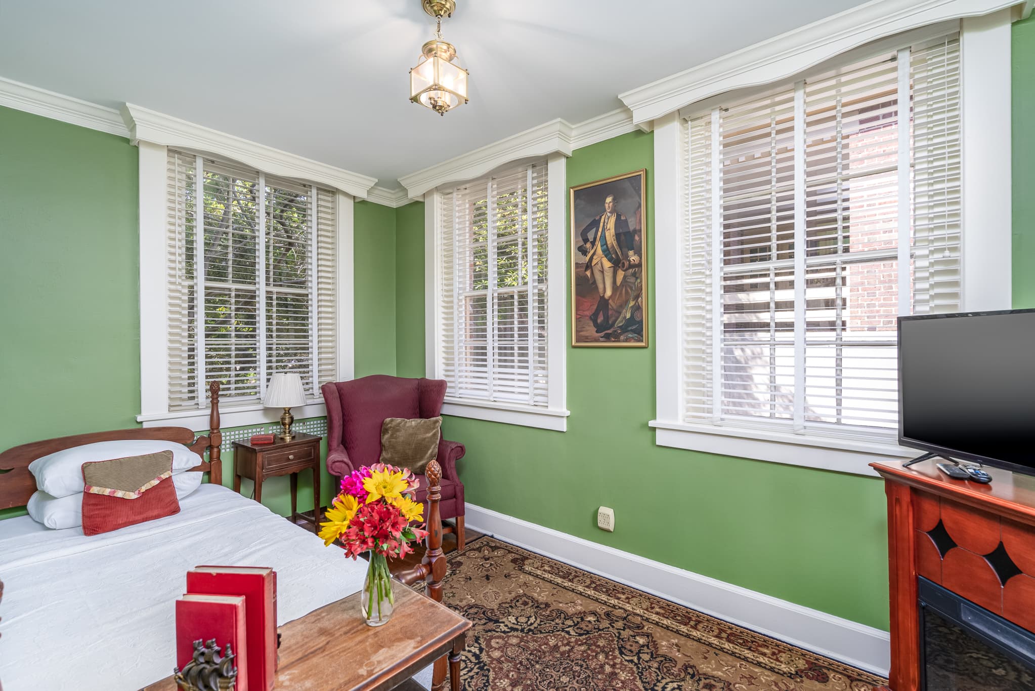 Second bedroom area with twin bed, cozy maroon armchair, bright windows and tv on wooden stand