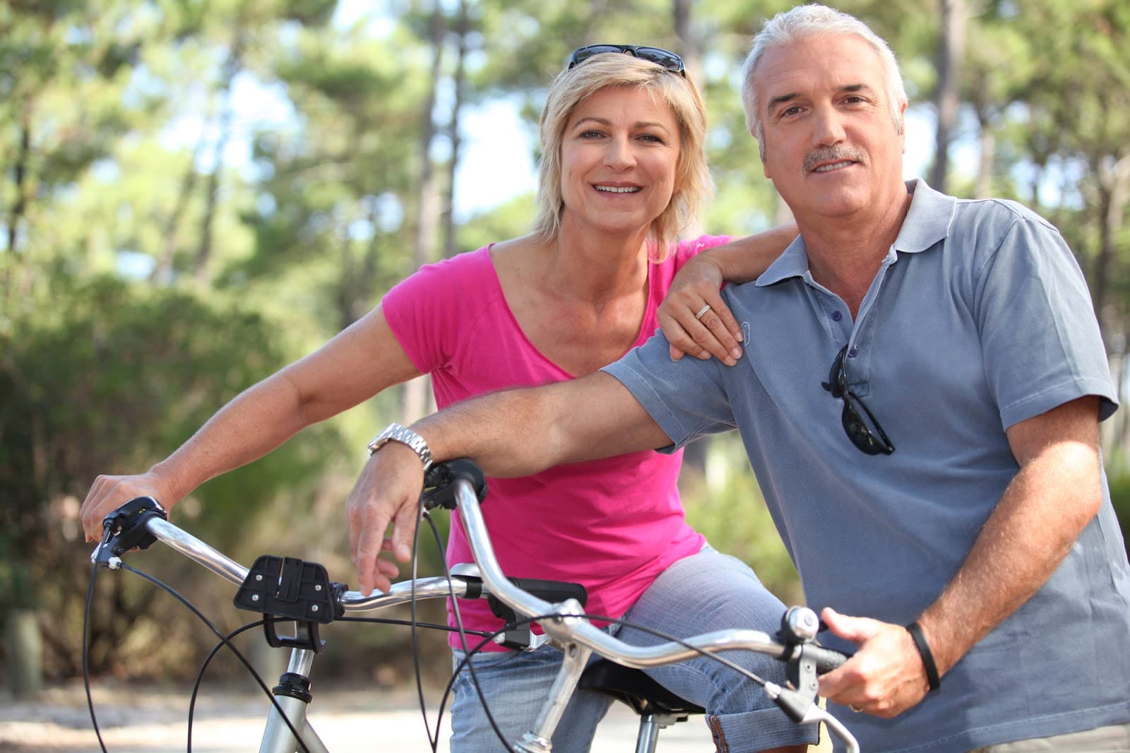 A smiling couple poses together with bicycles in a park setting.