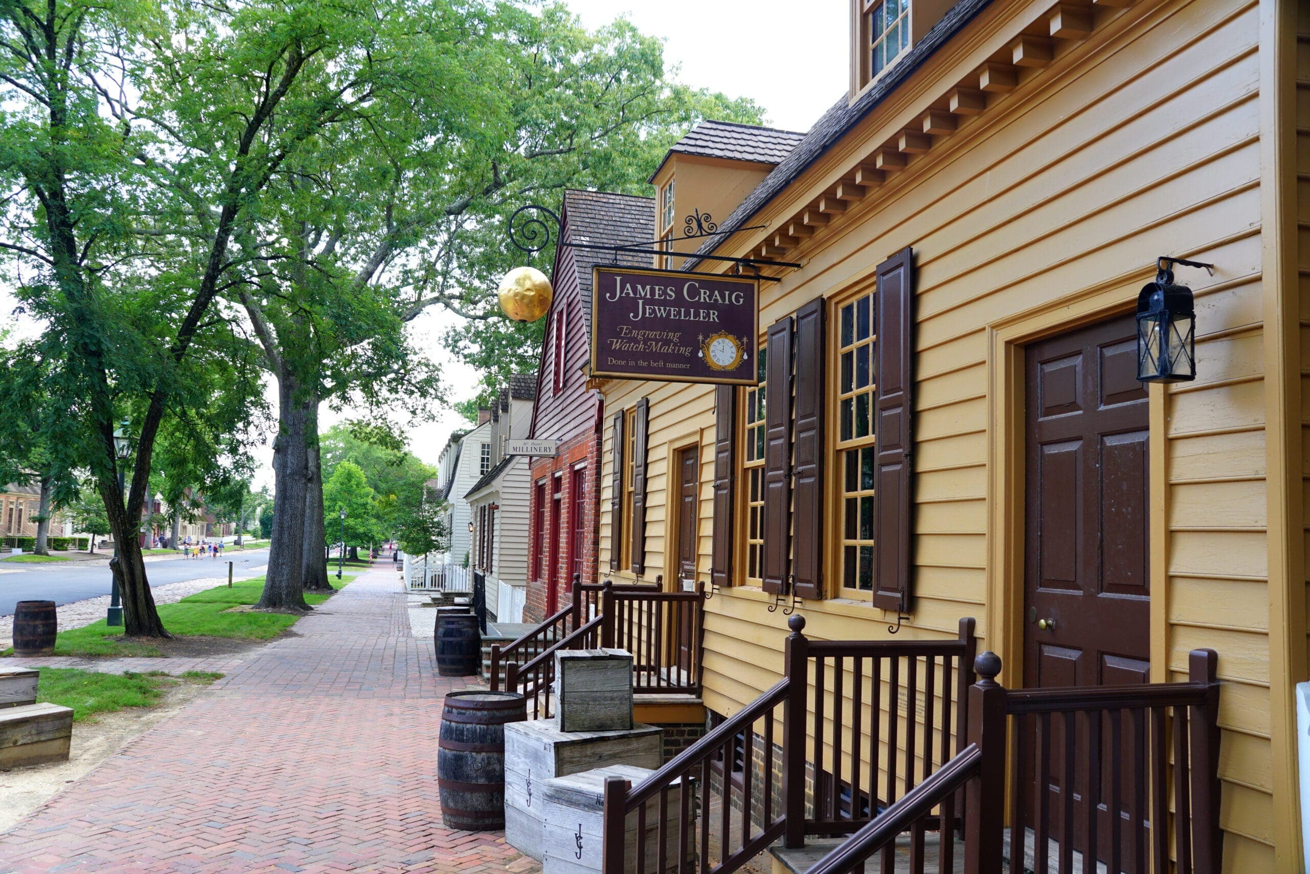 A street view of a historic building displaying a sign for James Craig Jeweller, with trees and a brick walkway nearby.