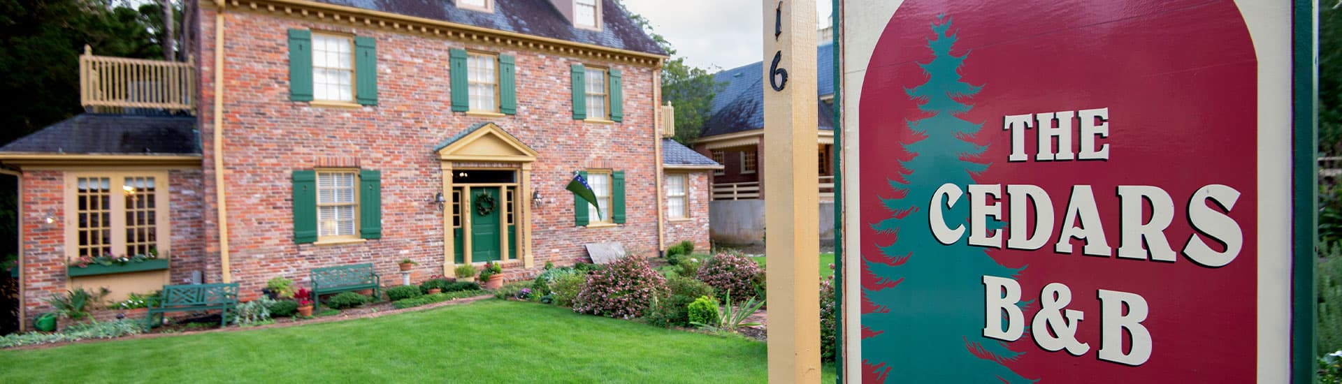A brick bed and breakfast with a sign reading "The Cedars B&B" in a landscaped yard.