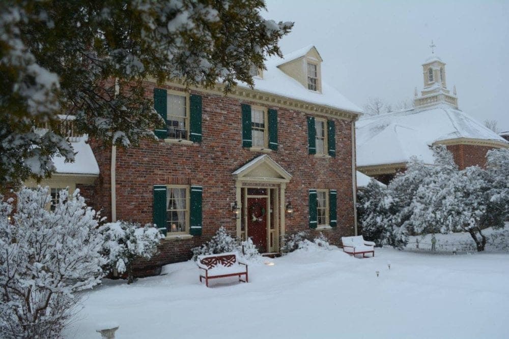 A brick house with green shutters surrounded by snow-covered trees and benches. A brick house with green shutters surrounded by snow-covered trees and benches.