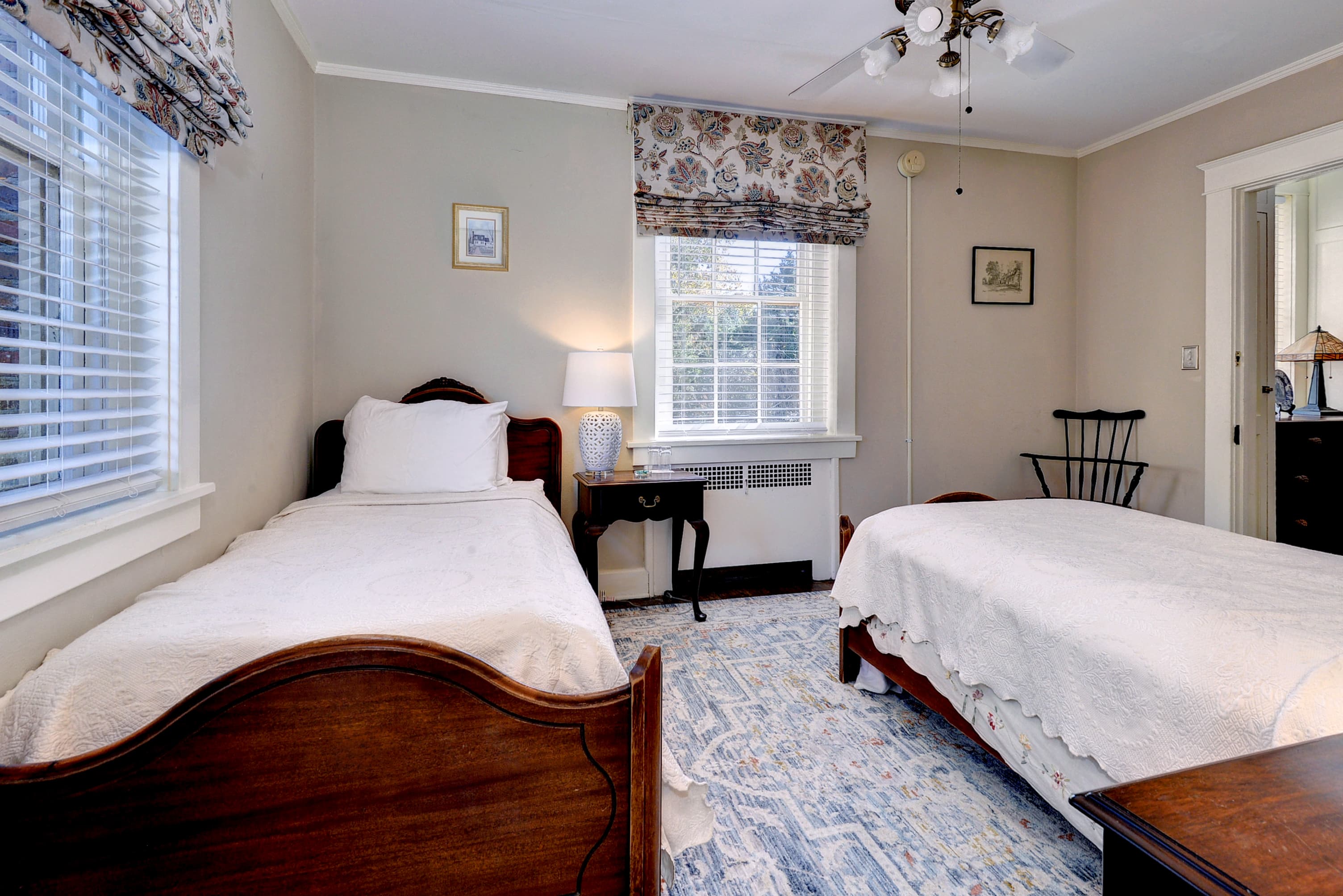 Cozy bedroom featuring two twin beds, a window with patterned curtains, and vintage decor.