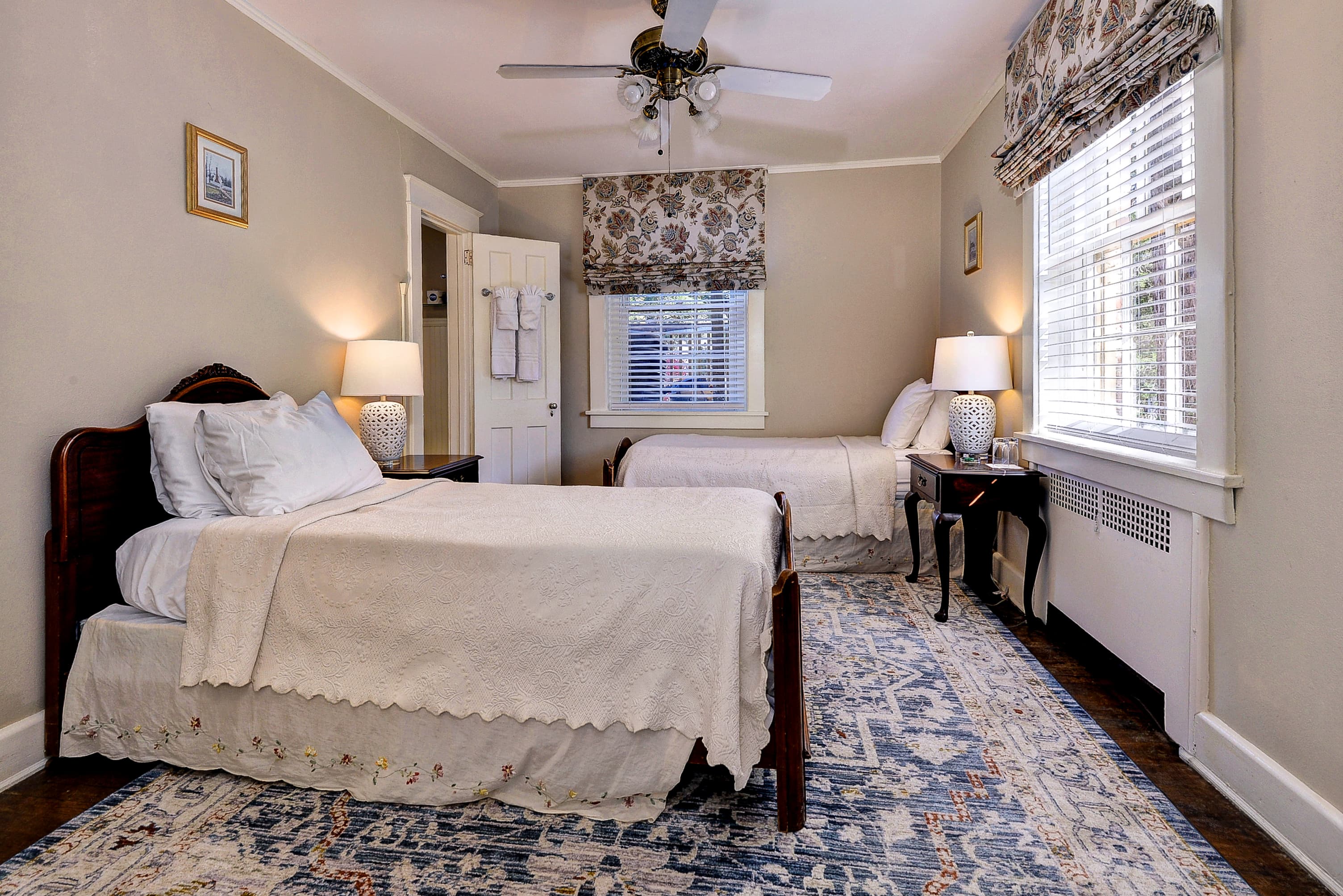 A cozy bedroom featuring two beds, bedside tables with lamps, and a decorative rug.