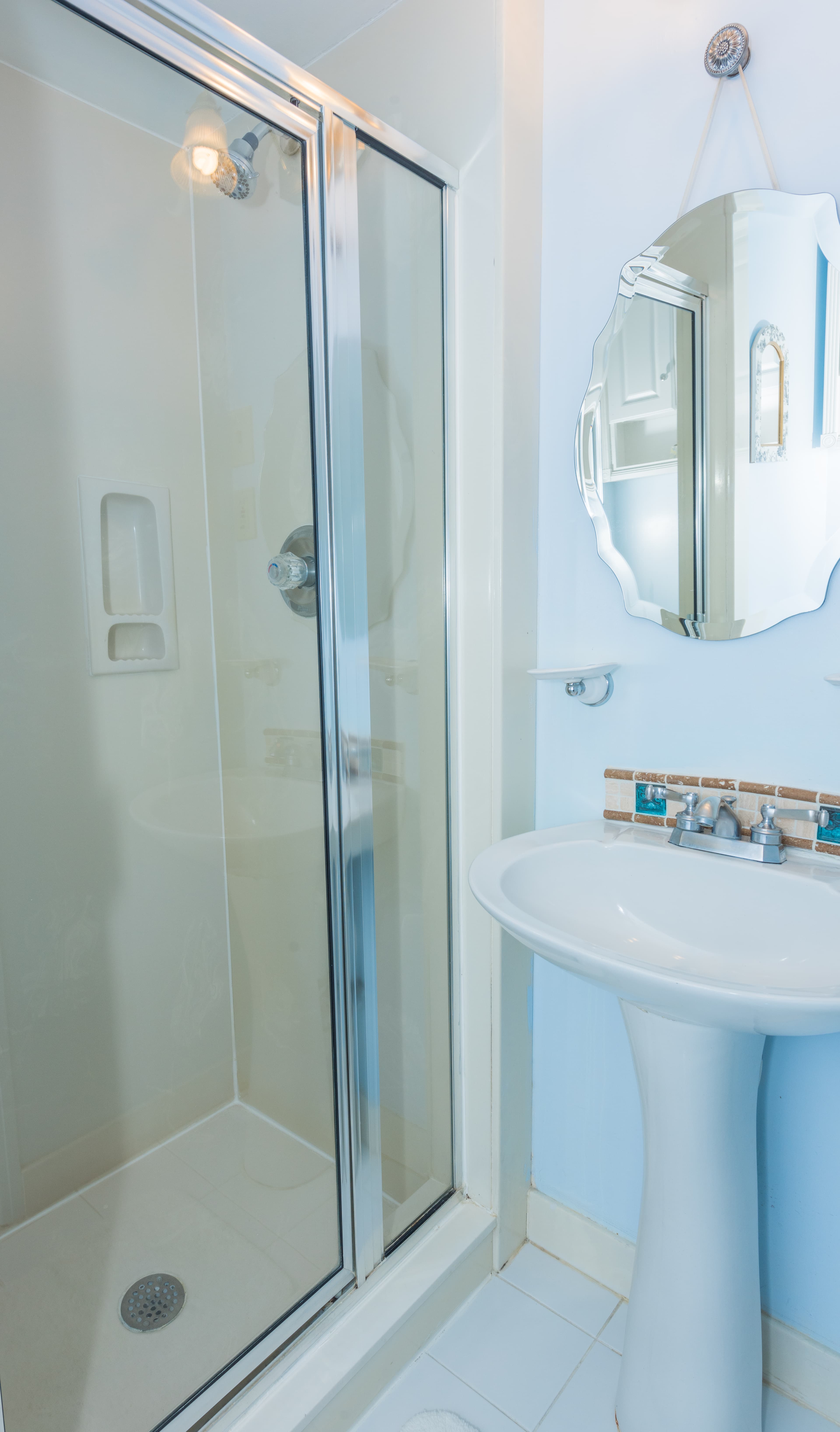 Bathroom with white walls and tile, walk in shower with glass door and white pedestal sink