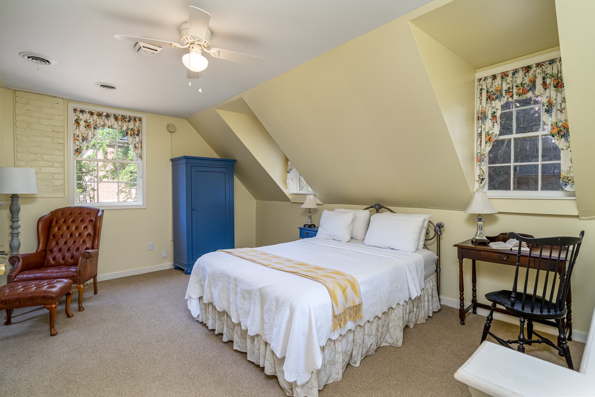 A cozy bedroom featuring a white bed, blue wardrobe, and a mix of vintage furniture.