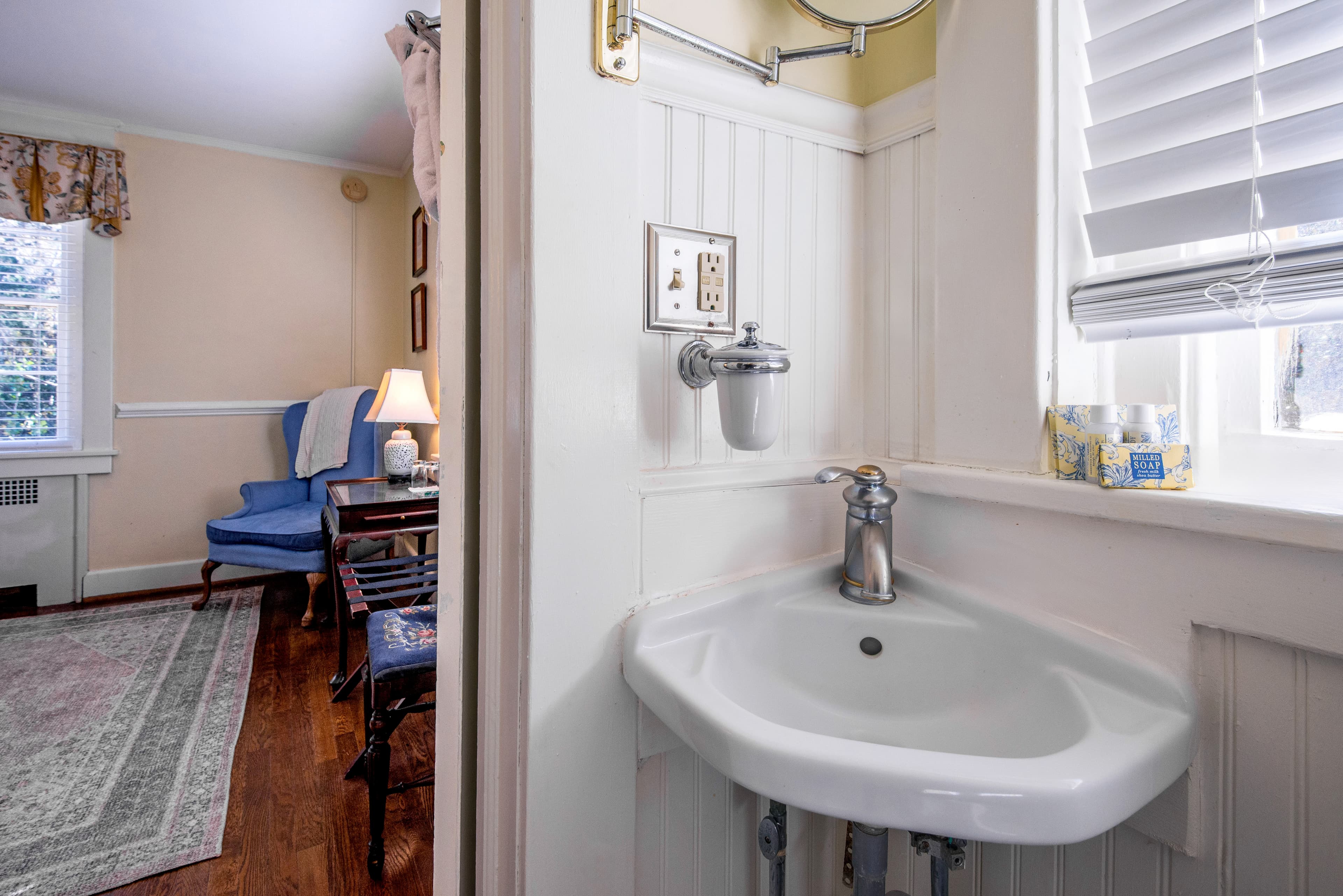 A small corner sink in a cozy room with a blue armchair and soft lighting.