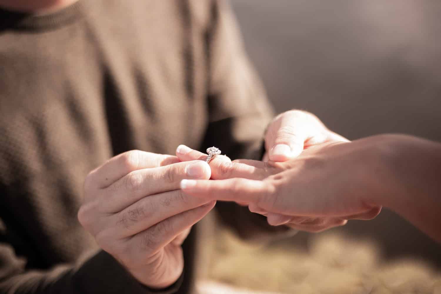 A person is placing a ring on another person's hand, symbolizing an engagement.