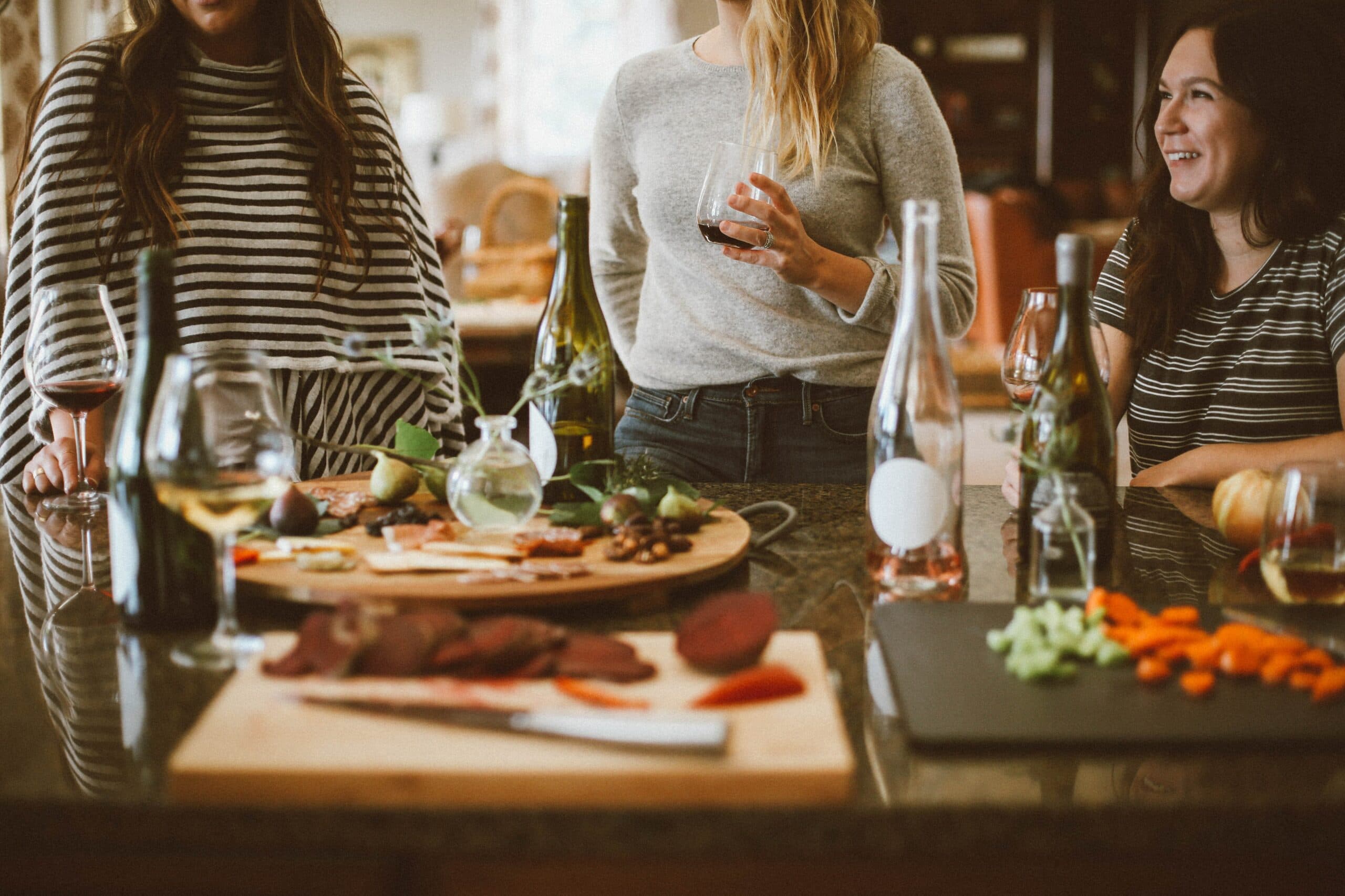 A group of friends enjoy wine and food together at a kitchen counter.