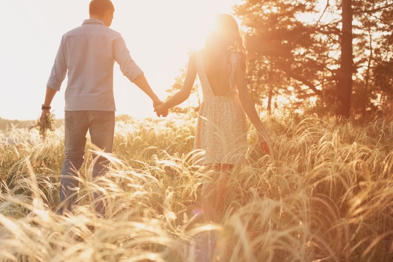 A couple walks hand in hand through a sunlit field. A couple walks hand in hand through a sunlit field.