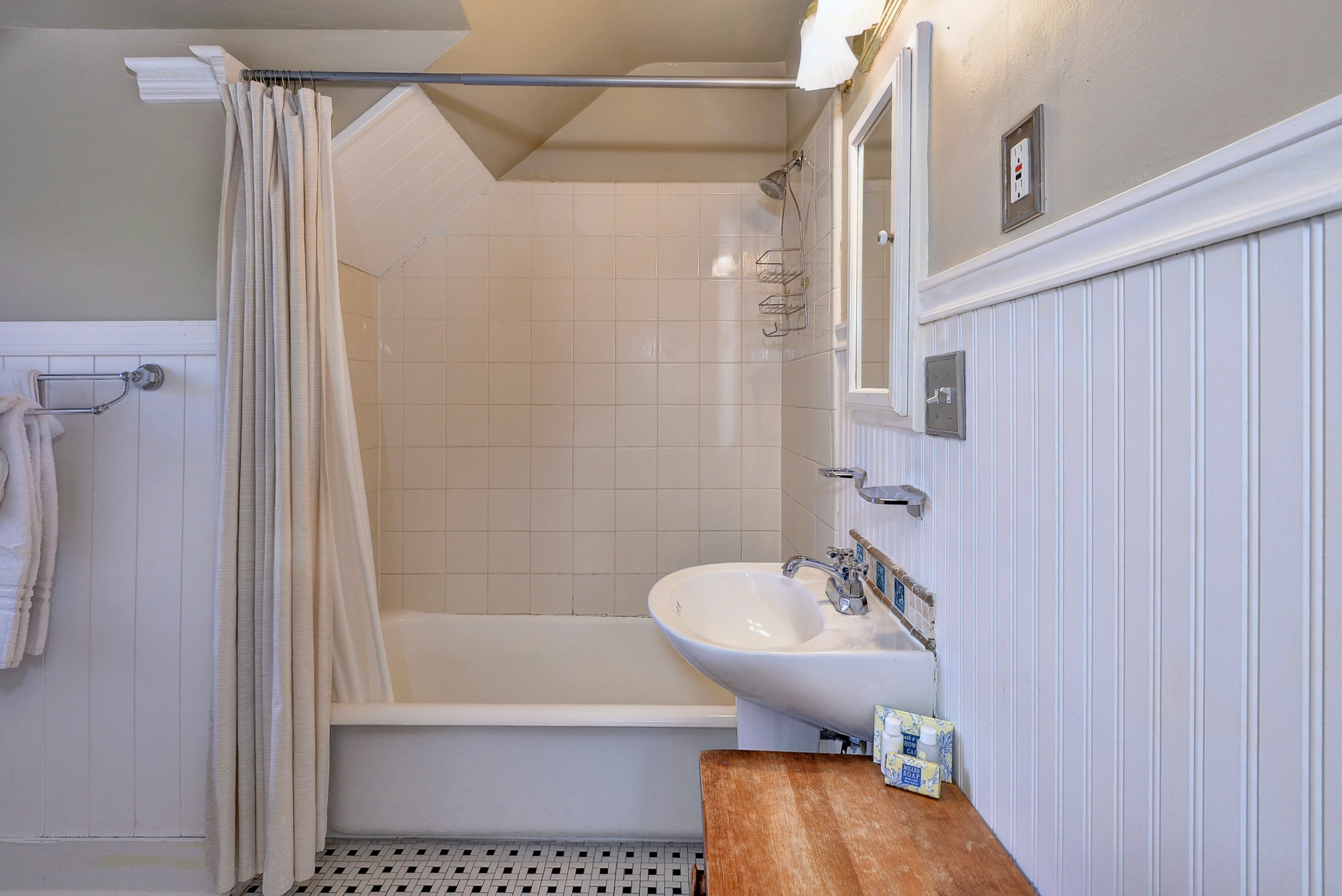 A neatly designed bathroom featuring a bathtub with a shower, a sink, and wooden accents.