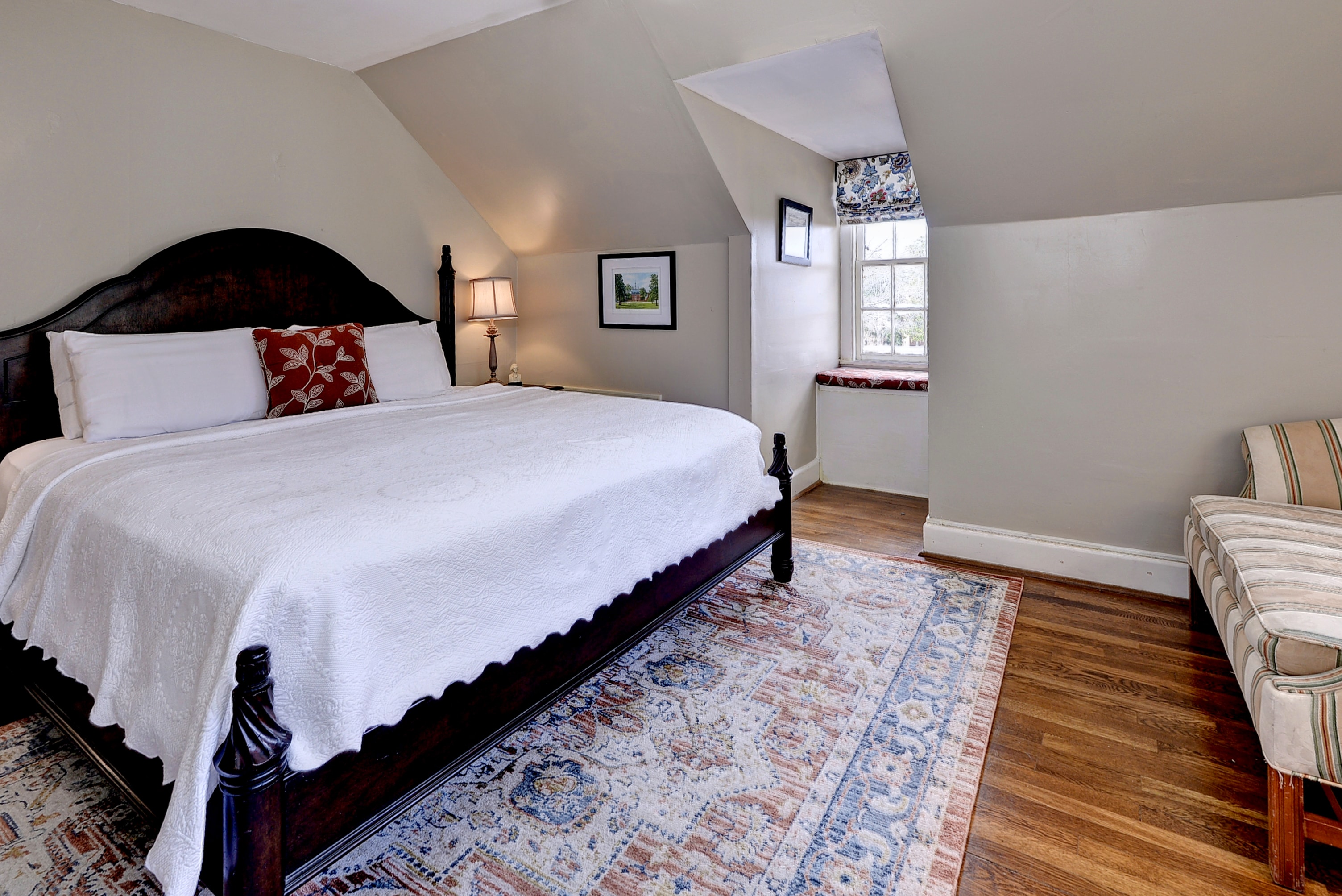 A cozy bedroom featuring a large bed, a patterned rug, and a small seating area by a window.