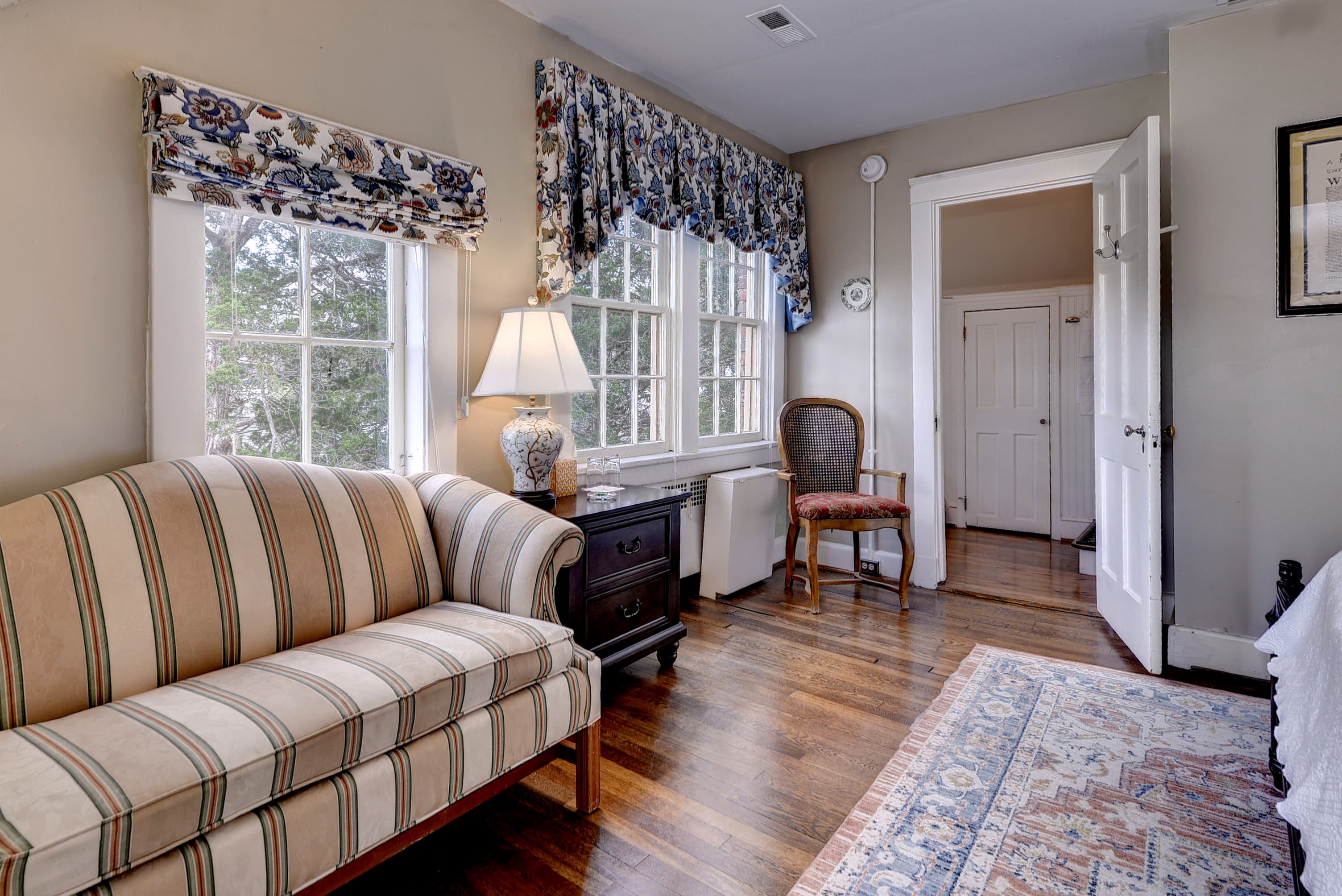 A cozy room featuring a striped sofa, a lamp, a wooden chair, and a patterned rug.