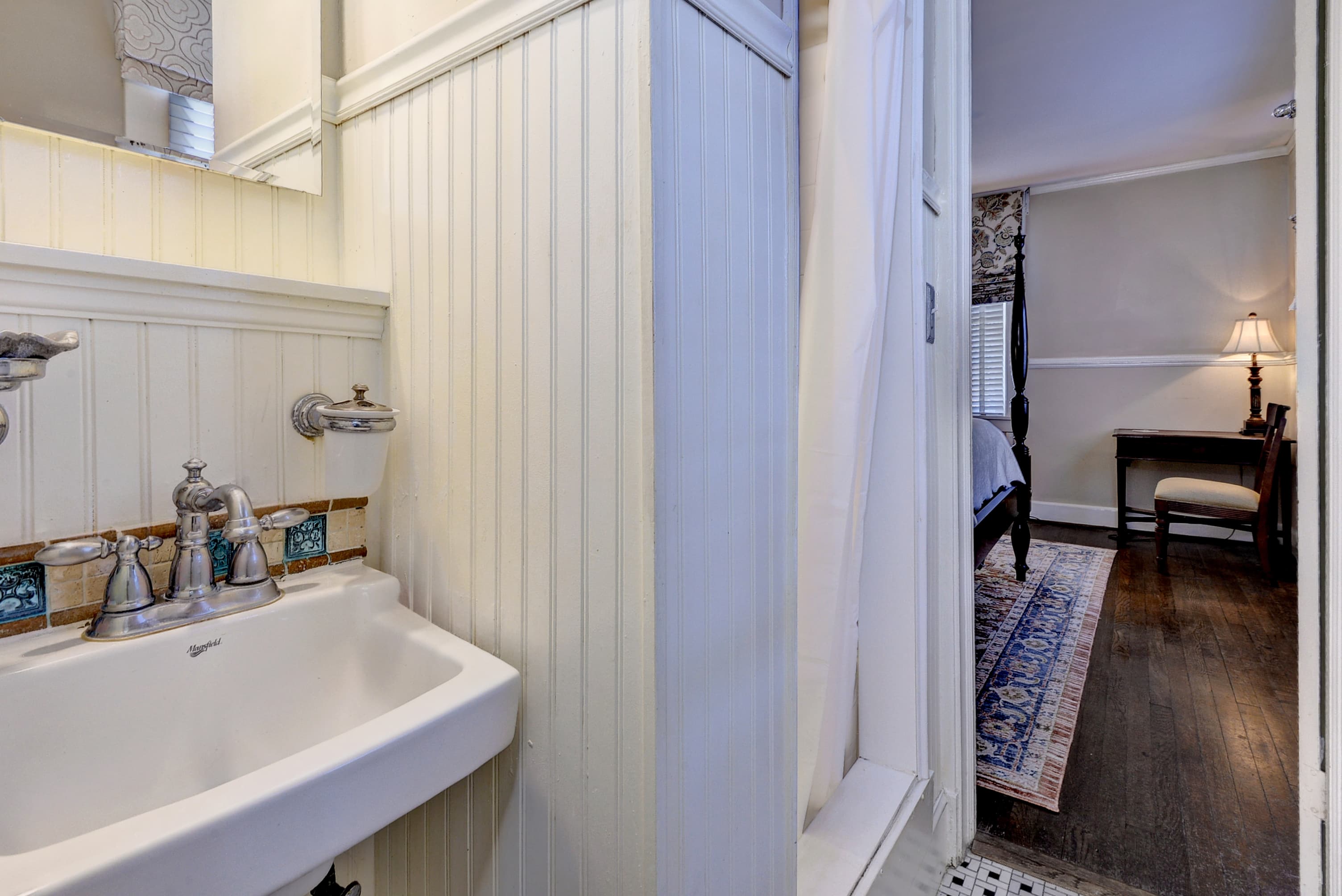 A small bathroom featuring a vintage sink and a glimpse into an adjacent room with a desk and chair.