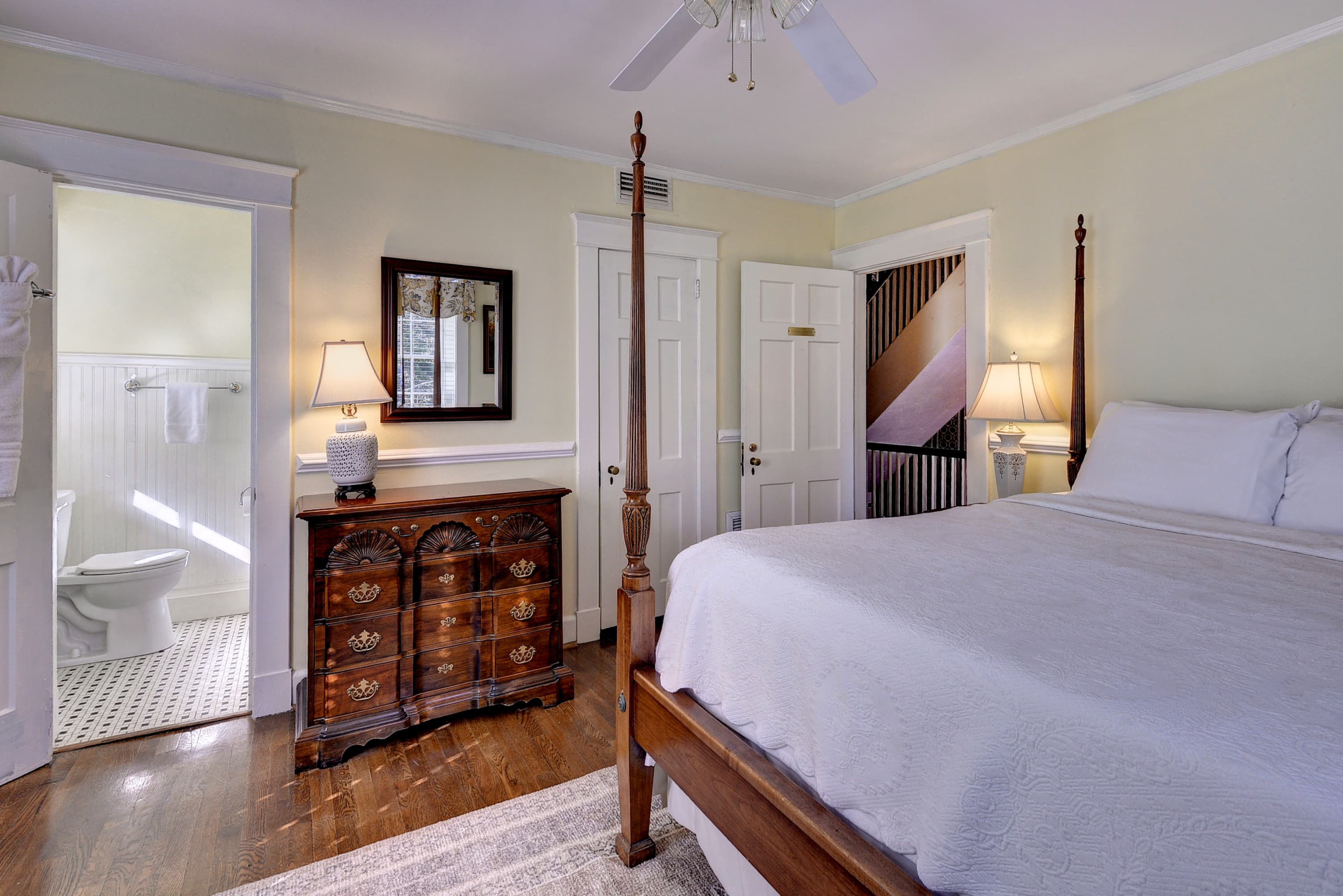 A cozy bedroom featuring a large bed, antique dresser, and an adjoining bathroom with a toilet.