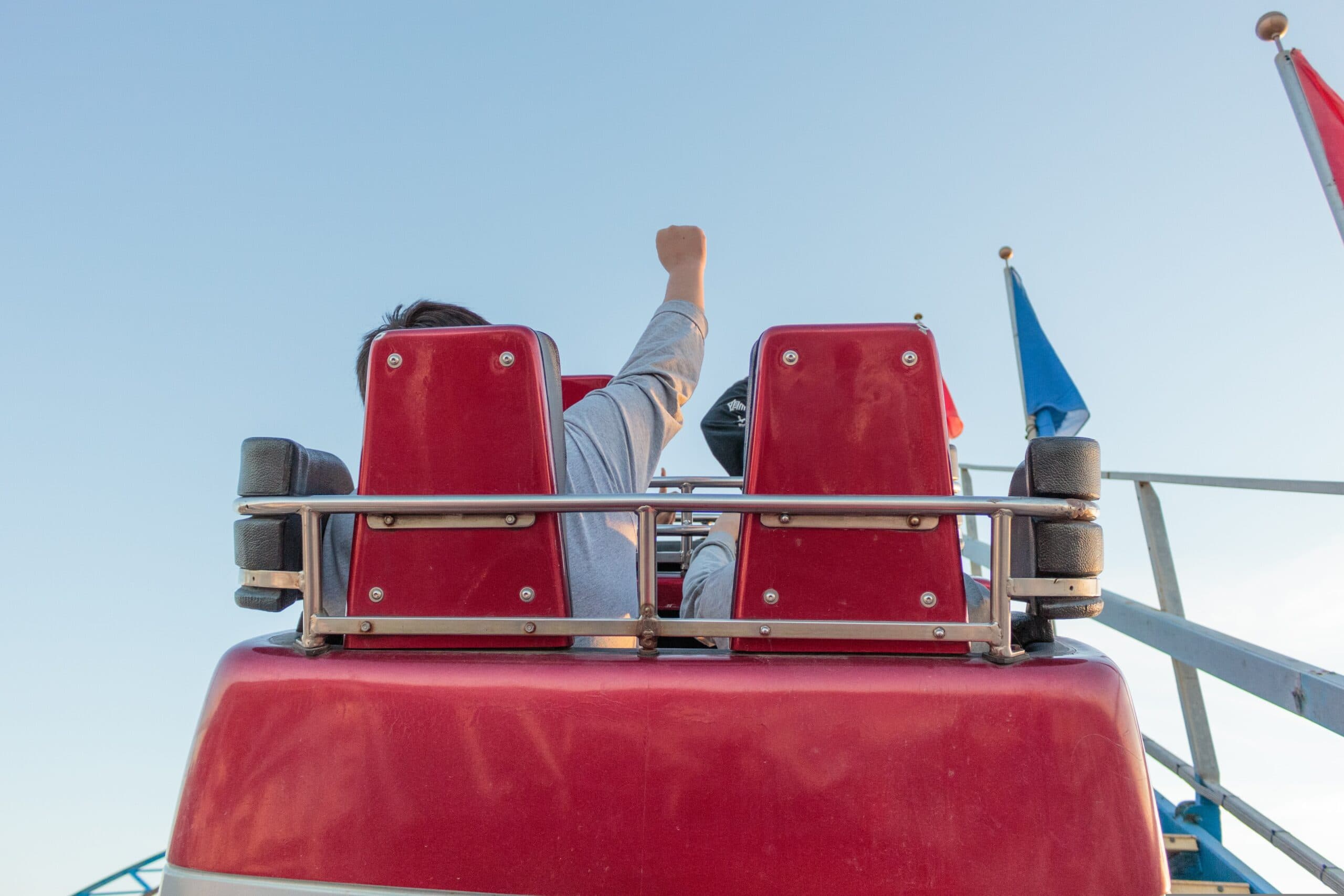 A person raises their fist in excitement while riding a roller coaster, viewed from behind.