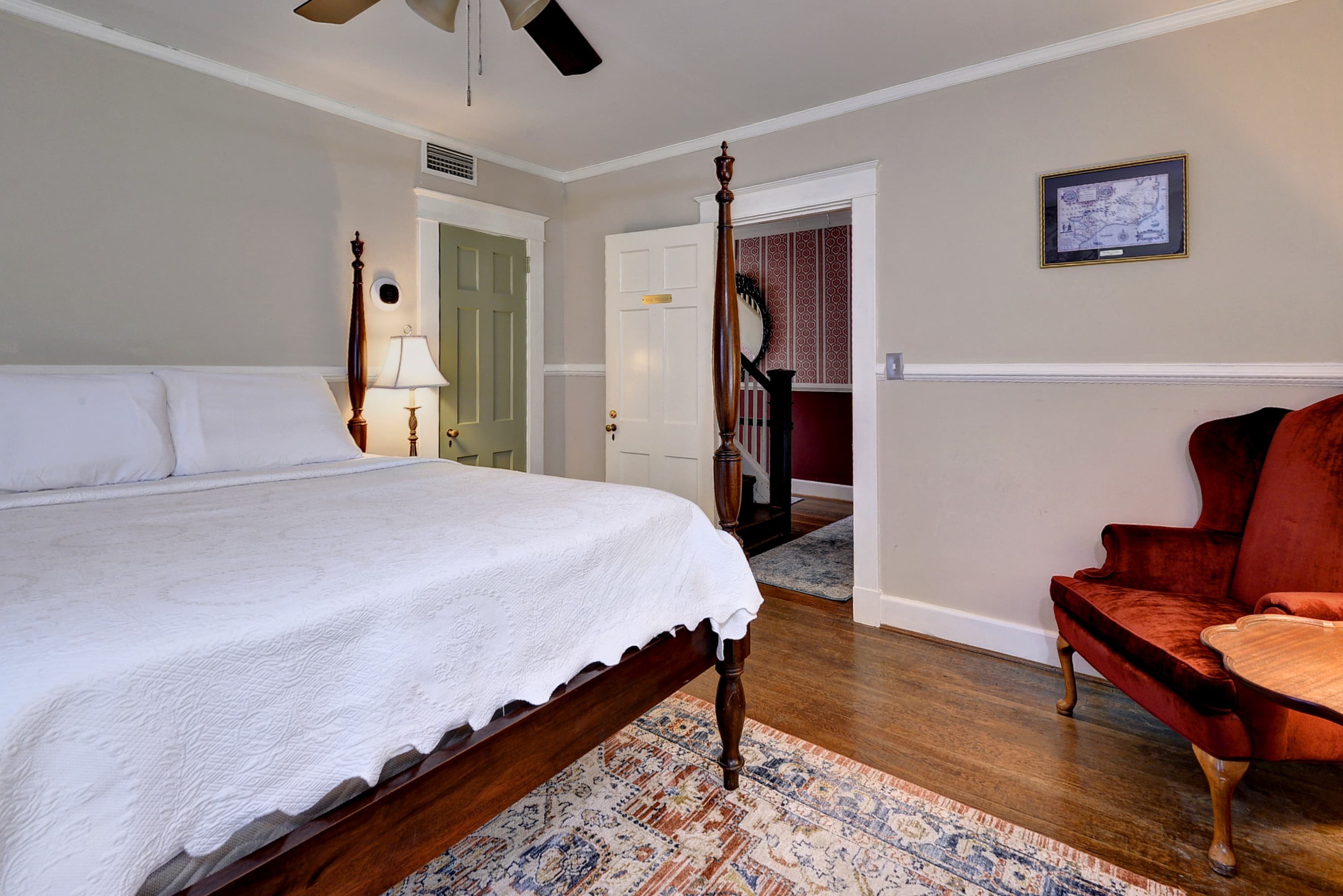 A cozy bedroom featuring a four-poster bed, a plush red chair, and wooden flooring.