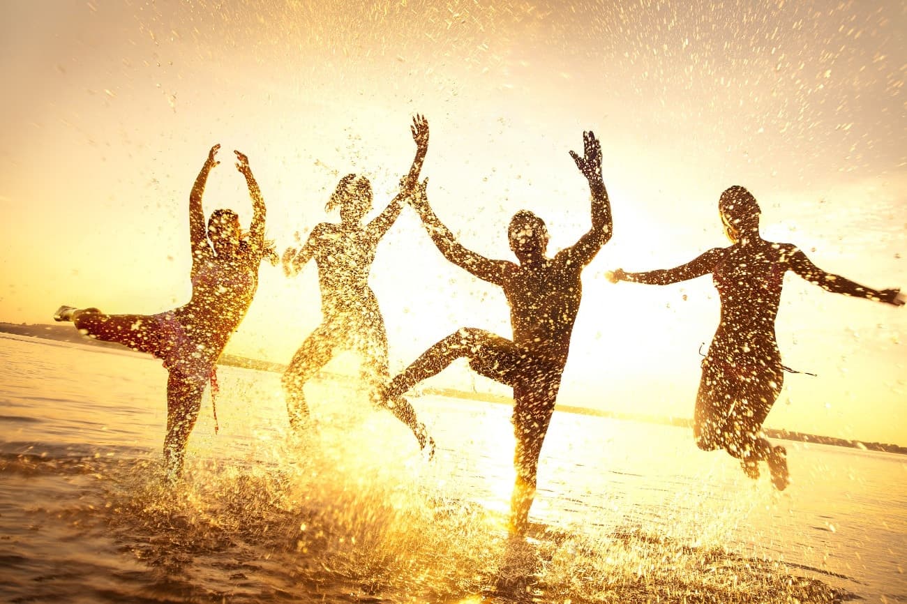 Five silhouetted figures joyfully splash in the water at sunset. Five silhouetted figures joyfully splash in the water at sunset.