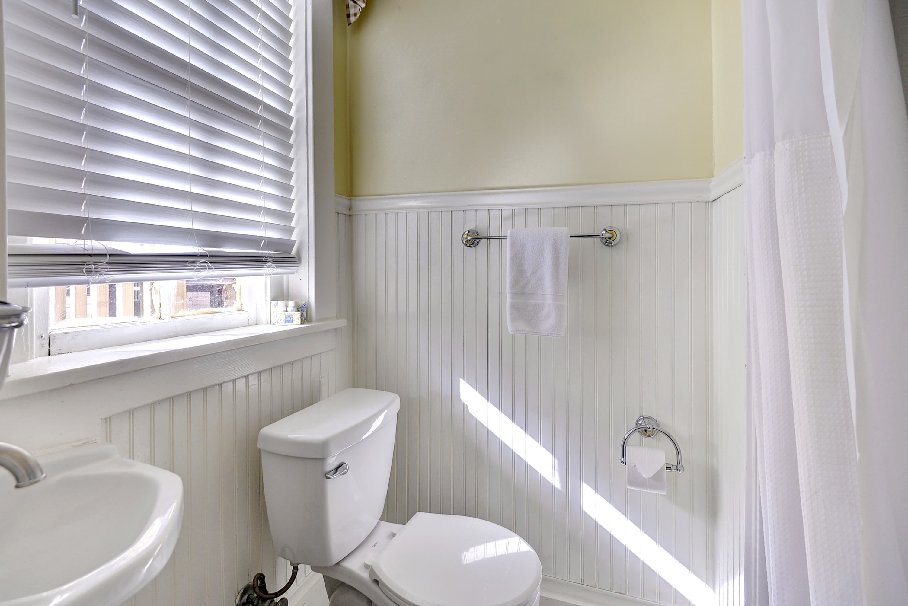 A bright bathroom featuring a toilet, sink, and shower with natural light streaming through the window.