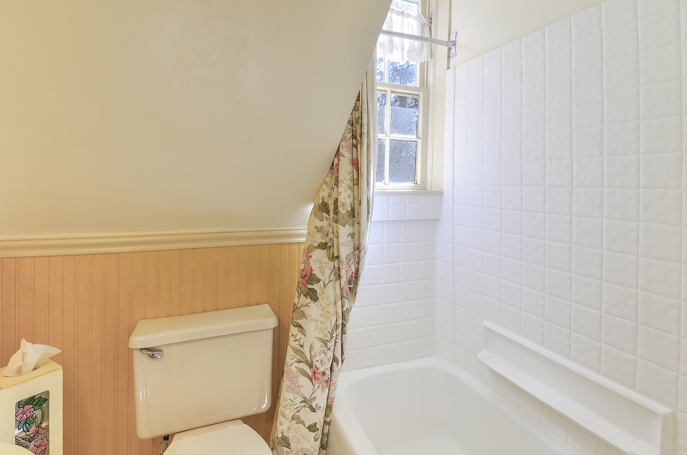A quaint bathroom featuring a bathtub, toilet, and window with natural light.