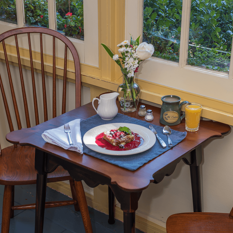 A cozy breakfast nook: The setting features a wooden table, chairs, and a large window overlooking greenery.
