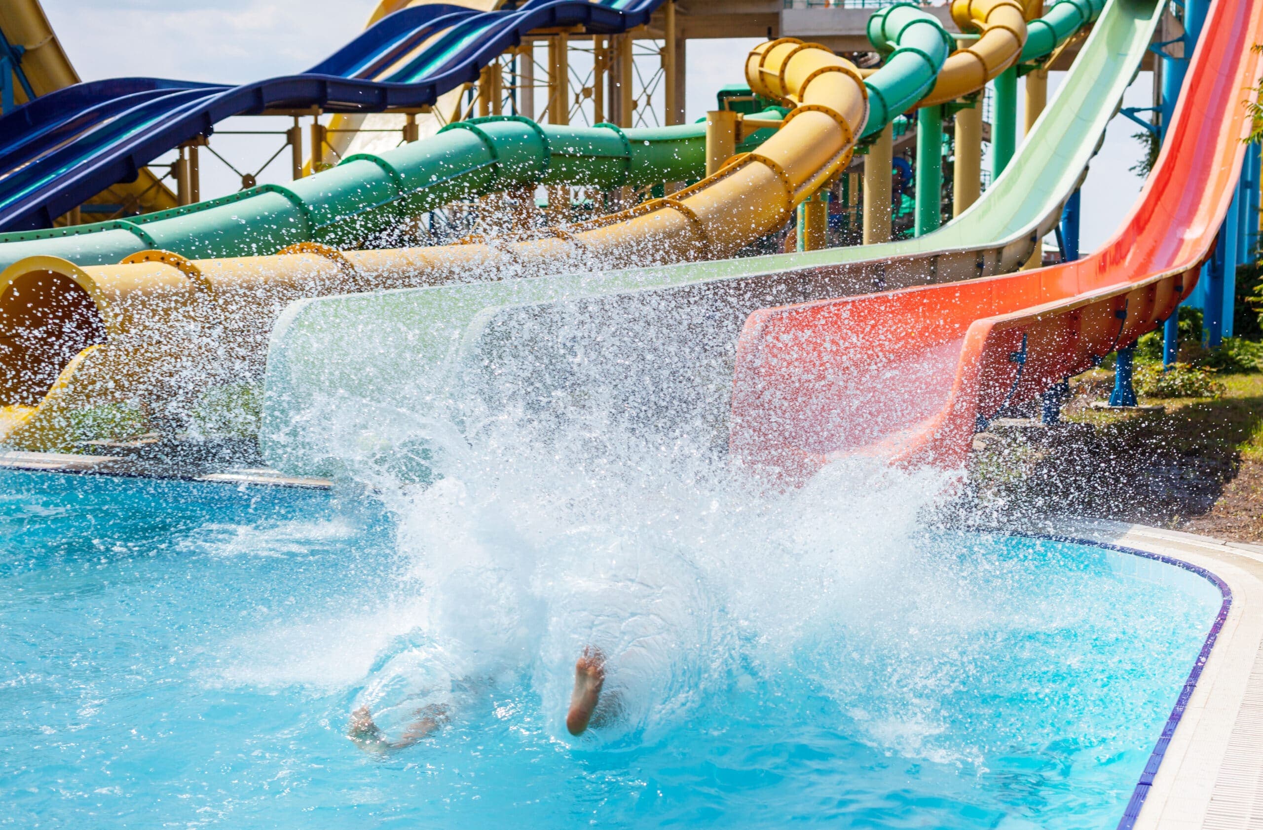 A person splashes into a pool after sliding down a colorful water slide.