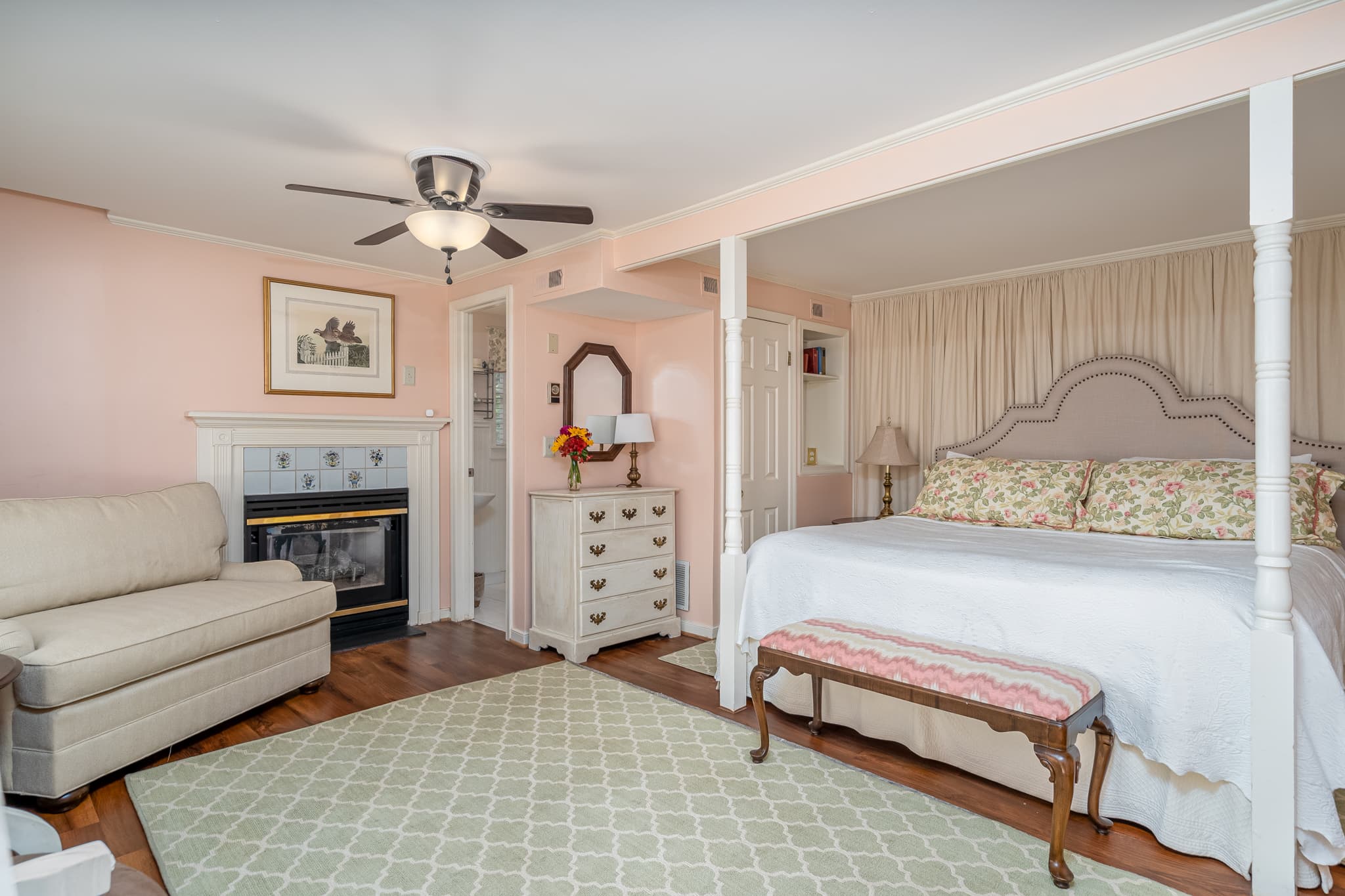 A cozy bedroom featuring a white bed, floral accents, a small sofa, and a decorative rug.