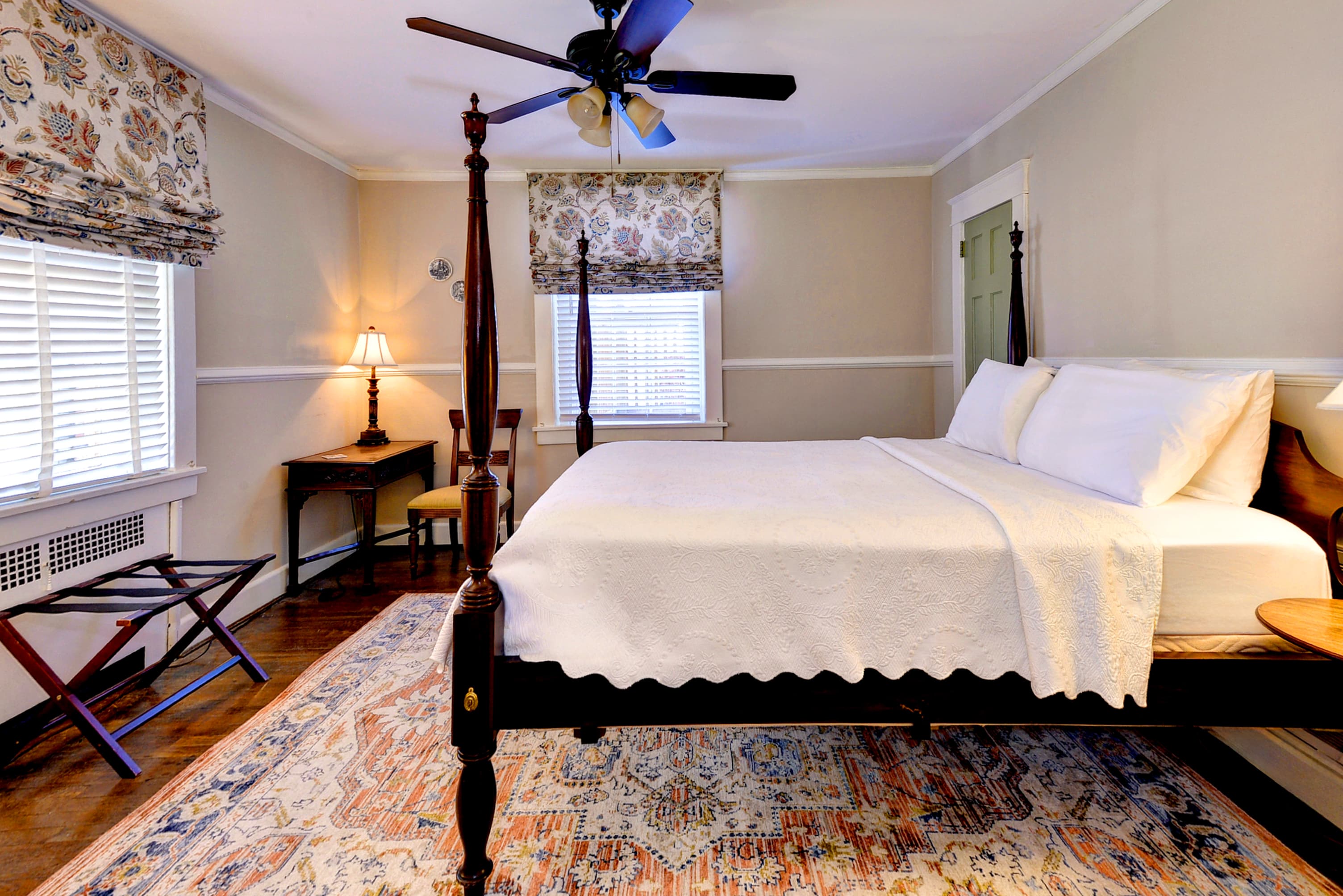 A cozy bedroom featuring a four-poster bed, desk, and decorative rug.