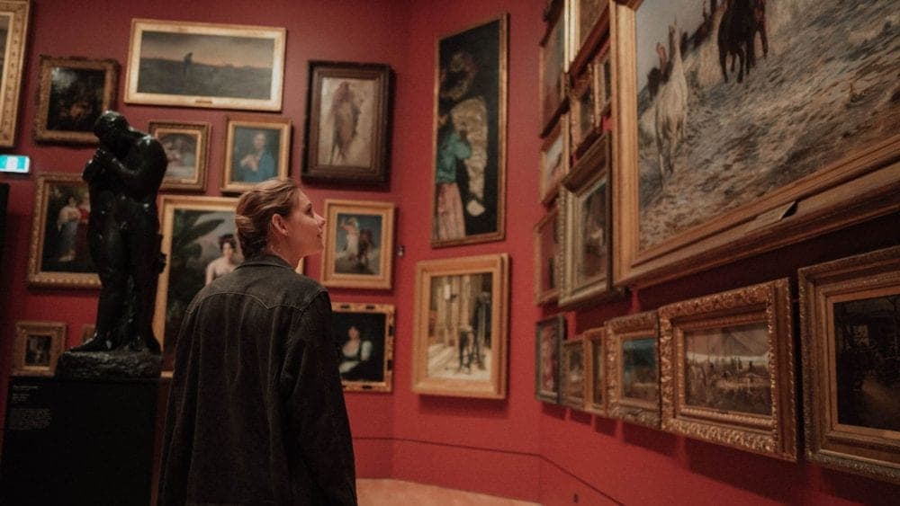 A person looks at various paintings and a statue in an art gallery. A person looks at various paintings and a statue in an art gallery.