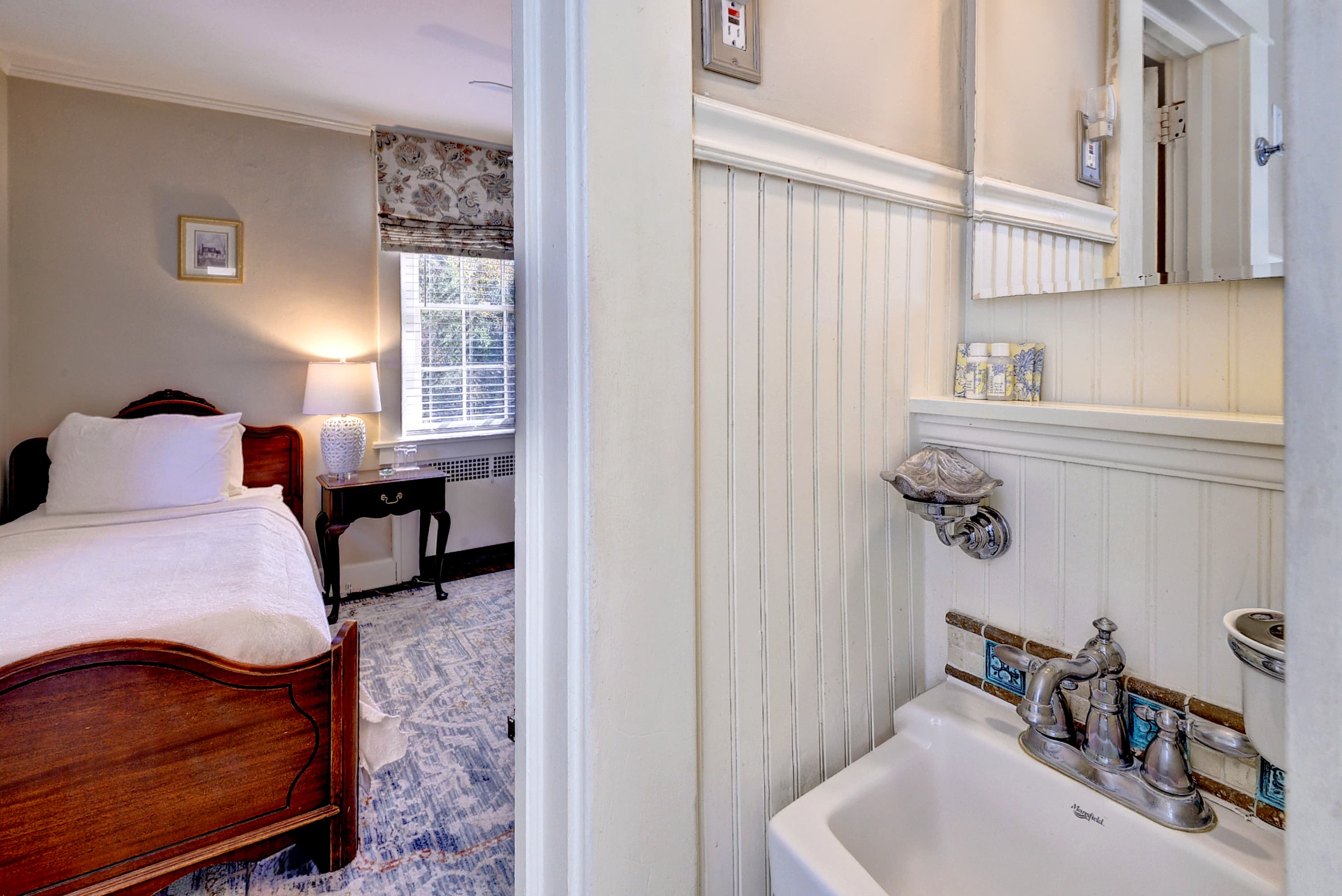 A cozy bedroom with a wooden bed and a sink in an adjoining bathroom.