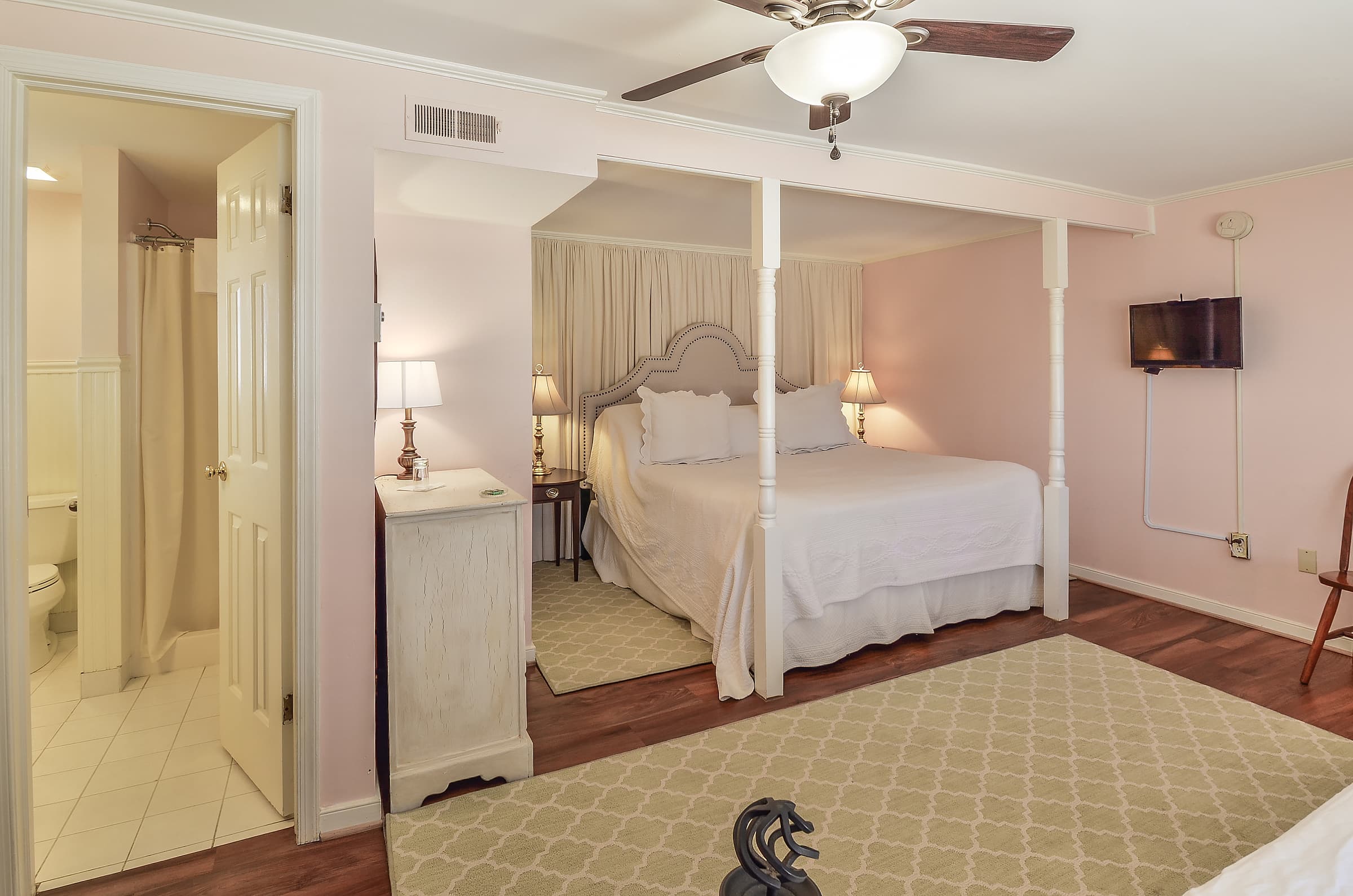 A cozy bedroom featuring a queen-sized bed, pink walls, and a small en-suite bathroom.