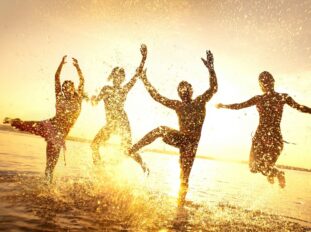 golden backlit silhouettes of people splashing in shallow water